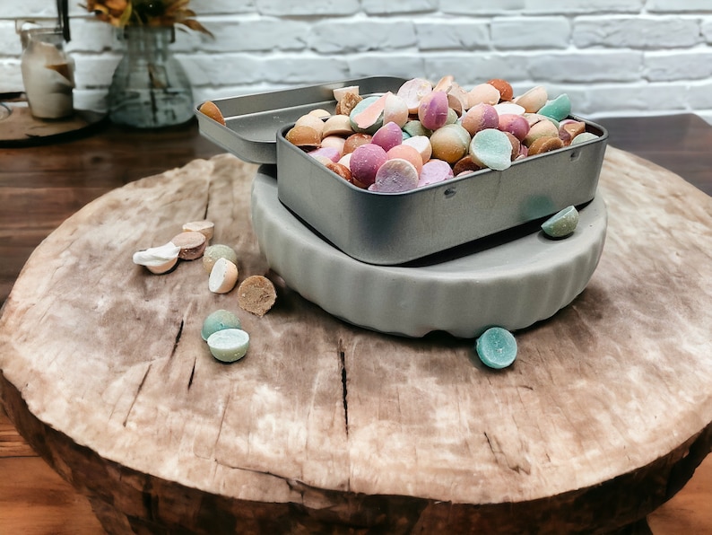 May include: A metal tin filled with colorful candy, sitting on a wooden surface. The candy is in the shape of small, round balls and is a variety of colors, including pink, green, yellow, and orange.