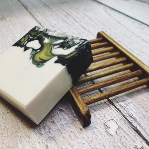 Op de afbeelding: Een witte en groene swirl zeepstaaf met een zwarte rand, rustend op een houten zeepbakje.