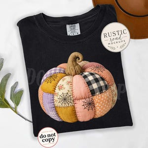 May include: A black t-shirt featuring a central graphic of a patchwork pumpkin. The pumpkin is composed of various fabric patterns including gingham, floral, polka dots, and spider web prints in shades of orange, purple, and tan with a brown stem.