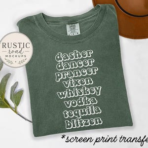 May include: A sage green t-shirt featuring white, wavy-font text listing the words: dasher, dancer, prancer, vixen, whiskey, vodka, tequila, blitzen. The shirt has a Comfort Colors brand label at the neck and is a screen print transfer.