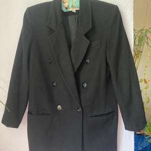 May include: A black double-breasted blazer featuring a notched lapel, long sleeves, and two front pockets. The garment is secured with four visible black buttons arranged in two columns, with a single button closure at the waist area.