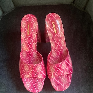 May include: A pair of pink and white plaid high-heeled mules with an open-toe design. The shoes feature a glossy finish and a block heel. The brand name Larroude is printed in gold lettering on the inner sole of each shoe.