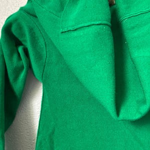 May include: A vivid green knit sweater, featuring a folded collar and a ribbed texture. The image provides a close-up view, emphasizing the fabric's details and the garment's design. The sweater's bright colour makes it a striking item.