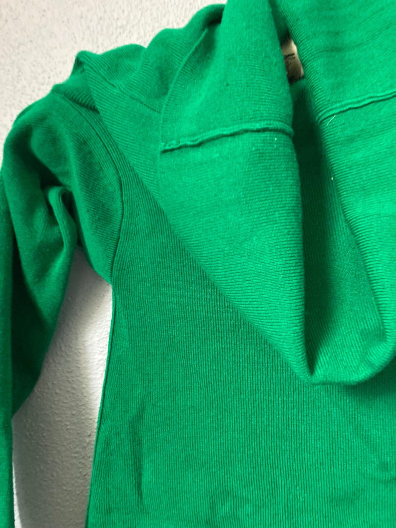 May include: A vivid green knit sweater, featuring a folded collar and a ribbed texture. The image provides a close-up view, emphasizing the fabric's details and the garment's design. The sweater's bright colour makes it a striking item.