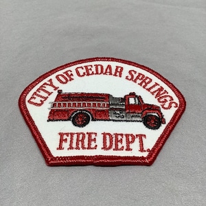 Może przedstawiać: Naszywka haftowana na biało-czerwono z tekstem "City of Cedar Springs Fire Dept." i ilustracją czerwonego wozu strażackiego.