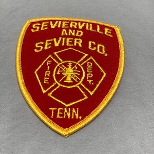 Puede incluir: Parche bordado rojo y dorado con el texto "Sevierville and Sevier Co. Tenn." y un símbolo de departamento de bomberos.
