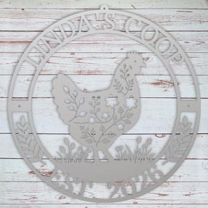 Decorative metal sign with a rooster design and 'Linda's Coop' text on a wooden background