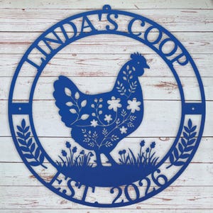Decorative blue metal sign with a rooster design and 'Linda's Coop' text on a wooden background.