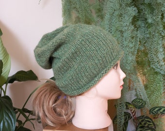 May include: A green knitted beanie with a slouchy fit. The beanie is made of a soft, textured yarn and has a simple, classic design.