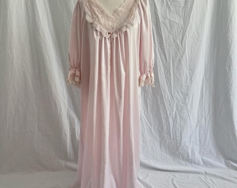 May include: A floor-length pale pink nightgown featuring a V-neckline with beige lace trim, a small central bow, and three-quarter length sleeves with ruffled lace cuffs. The garment has a loose, flowing silhouette and a smooth, satin-like finish.
