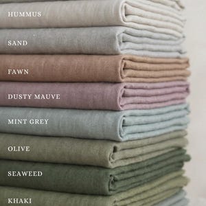 May include: A vertical stack of folded fabric swatches in various colors labeled Oatmeal, Hummus, Sand, Fawn, Dusty Mauve, Mint Grey, Olive, Seaweed, Khaki, and Sage. Each piece of fabric has a visible woven texture and is neatly layered.