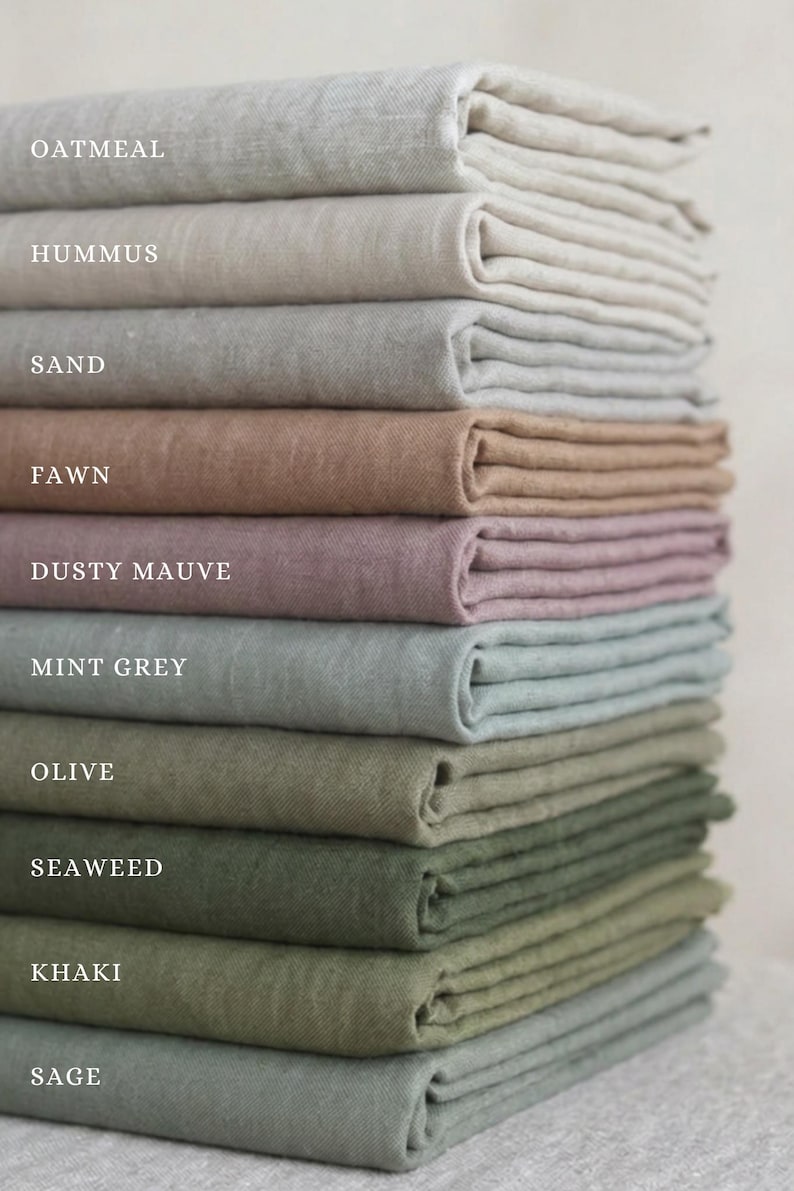 May include: A vertical stack of folded fabric swatches in various colors labeled Oatmeal, Hummus, Sand, Fawn, Dusty Mauve, Mint Grey, Olive, Seaweed, Khaki, and Sage. Each piece of fabric has a visible woven texture and is neatly layered.