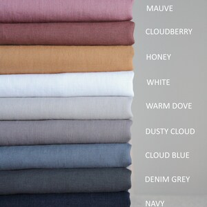 Op de afbeelding: Een stapel van 12 stofstalen in verschillende kleuren, waaronder blush roze, mauve, cloudberry, honing, wit, warm grijs, stoffig grijs, wolk blauw, denim grijs, marineblauw en off black.