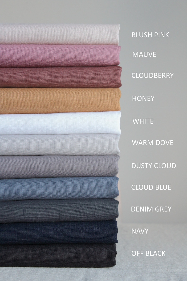 Op de afbeelding: Een stapel van 12 stofstalen in verschillende kleuren, waaronder blush roze, mauve, cloudberry, honing, wit, warm grijs, stoffig grijs, wolk blauw, denim grijs, marineblauw en off black.