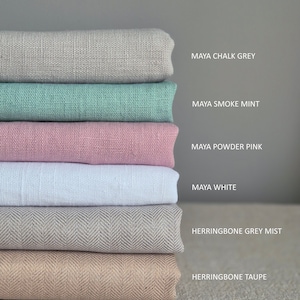 Op de afbeelding: Een stapel stofstalen in verschillende kleuren en texturen, waaronder Maya krijtgrijs, Maya rookmunt, Maya poederroze, Maya wit, herringbone grijs mist en herringbone taupe.