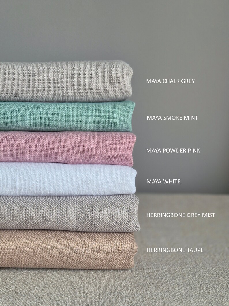 Op de afbeelding: Een stapel stofstalen in verschillende kleuren en texturen, waaronder Maya krijtgrijs, Maya rookmunt, Maya poederroze, Maya wit, herringbone grijs mist en herringbone taupe.