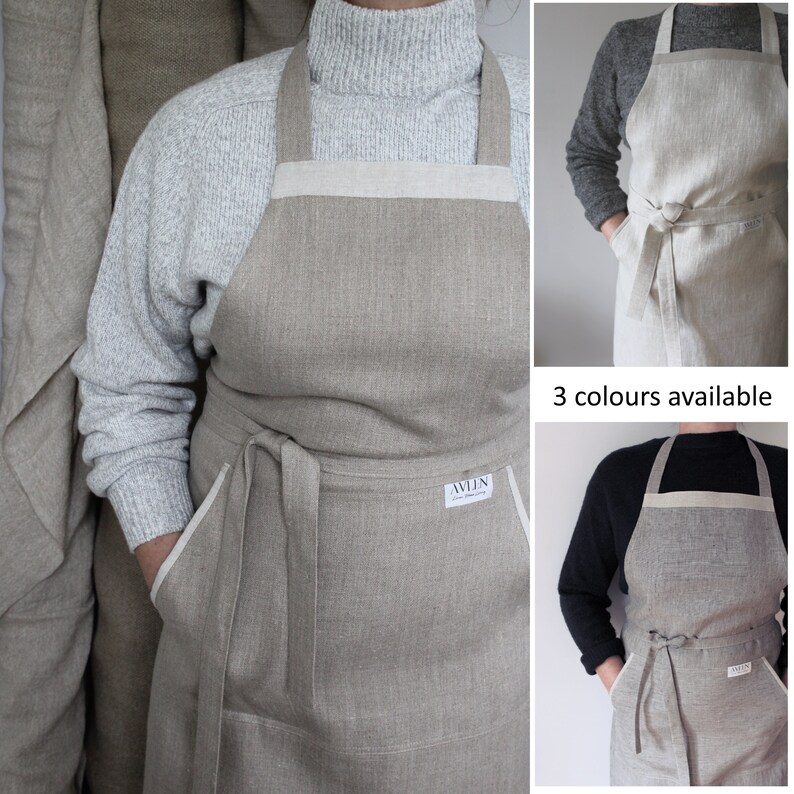May include: A beige linen apron with white trim and two pockets. The apron has adjustable straps and a tie at the waist. The apron is made by the company "AVLN".