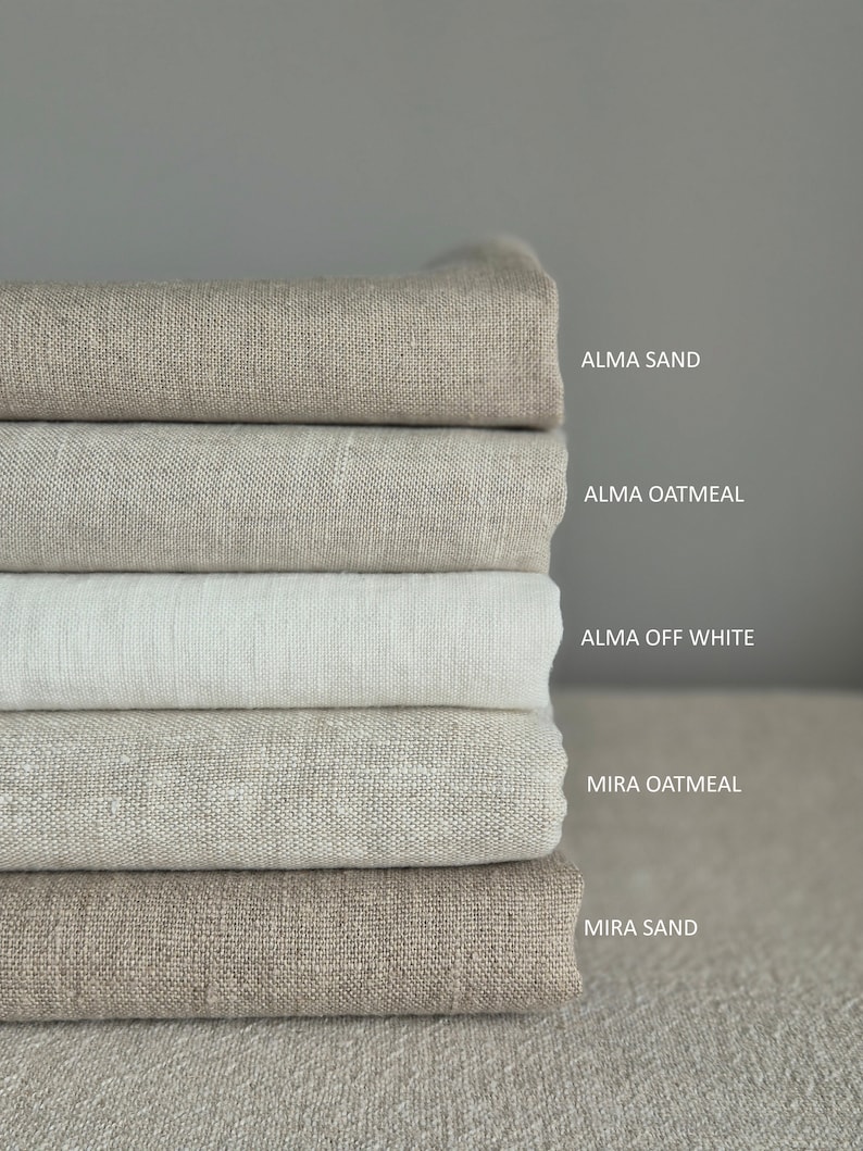 Op de afbeelding: Vijf verschillende tinten linnen stof gestapeld op elkaar. De kleuren zijn: Alma Sand, Alma Oatmeal, Alma Off White, Mira Oatmeal en Mira Sand.