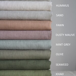 Op de afbeelding: Een stapel van tien stofstalen in verschillende tinten beige, bruin, groen en grijs. De stalen zijn gelabeld met de volgende namen: Oatmeal, Hummus, Sand, Fawn, Dusty Mauve, Mint Grey, Olive, Seaweed, Khaki en Sage.