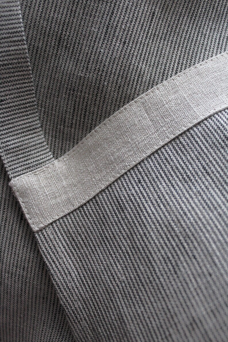 May include: Close-up of a grey and white striped fabric with a white band across the middle. The fabric has a textured, woven look.