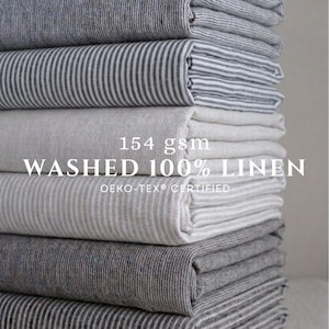May include: A stack of folded fabric pieces in various shades of gray and white, featuring striped and solid patterns. The text 154 gsm WASHED 100% LINEN OEKO-TEX CERTIFIED is overlaid on the center of the stack of folded textile materials.