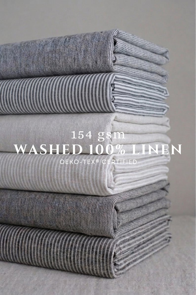 May include: A stack of folded fabric pieces in various shades of gray and white, featuring striped and solid patterns. The text 154 gsm WASHED 100% LINEN OEKO-TEX CERTIFIED is overlaid on the center of the stack of folded textile materials.