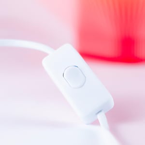 Close-up of a white inline switch with a rectangular button, connected to a white cord