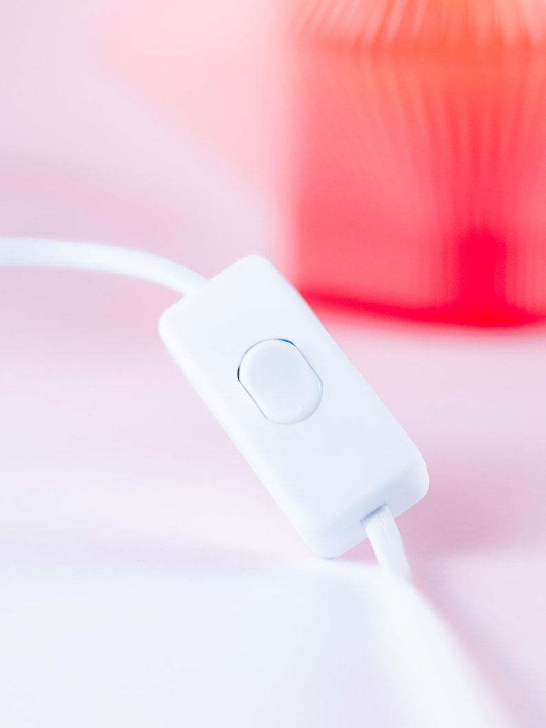 Close-up of a white inline switch with a rectangular button, connected to a white cord