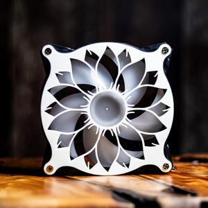 May include: A decorative fan with a white floral design on a black frame. The fan blades are visible through the openwork pattern. The fan is on a wooden surface.