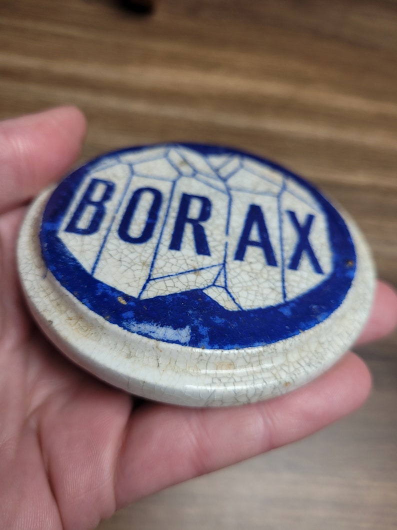 May include: A white ceramic lid with a blue border and the word "BORAX" printed in blue letters. The lid has a cracked glaze.