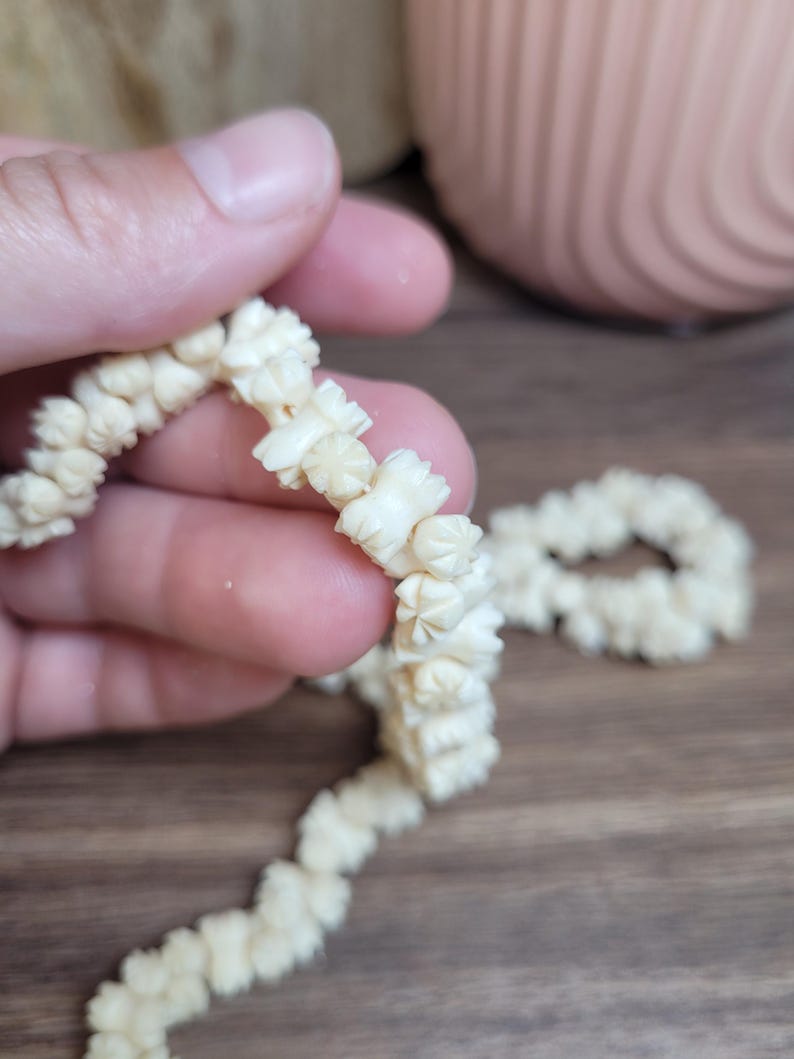 May include: A white, carved bone necklace with a flower design. The necklace is made of small, individual pieces of bone that are strung together.