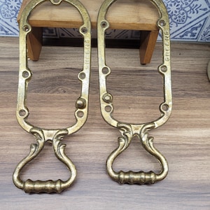 Puede incluir: Dos tiradores de puerta de metal antiguo de color dorado con diseños ornamentados y un asa de bucle. El tirador de la derecha tiene la palabra "GREENING" en relieve.