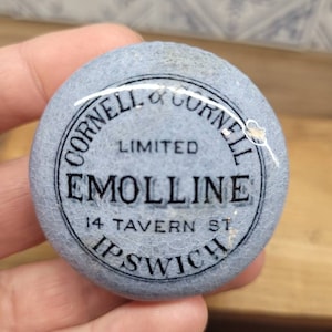 Puede incluir: Una tapa de tarro de cerámica azul y blanca con el texto "Cornell & Cornell Limited Emoline 14 Tavern St Ipswich" en letras negras.