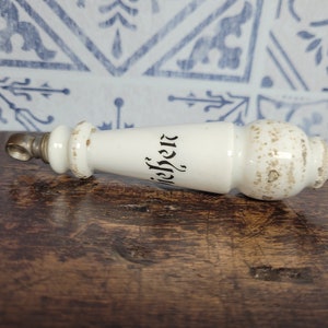 May include: White ceramic bottle stopper with a silver cap and the word "Nieber" written in black on the side.