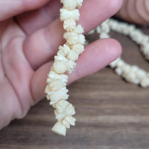 May include: A white carved bone necklace with intricate floral designs. Each bead is unique and features a different pattern.