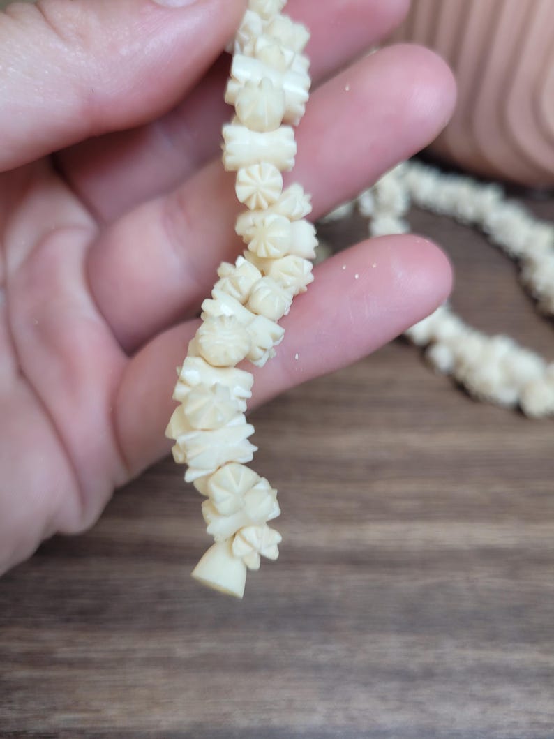 May include: A white carved bone necklace with intricate floral designs. Each bead is unique and features a different pattern.