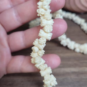May include: A long strand of white carved bone beads, each bead is shaped like a flower with a star in the center.