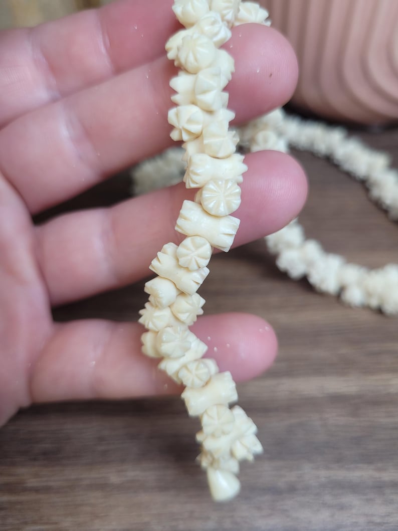 May include: A long strand of white carved bone beads, each bead is shaped like a flower with a star in the center.