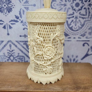 Peut inclure: Un pot en céramique blanche avec un motif floral décoratif. Le pot a un motif en treillis et un couvercle avec un bouton sur le dessus.
