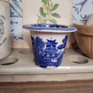 May include: A small blue and white ceramic planter with a blue and white floral design. The planter is sitting on a white shelf.