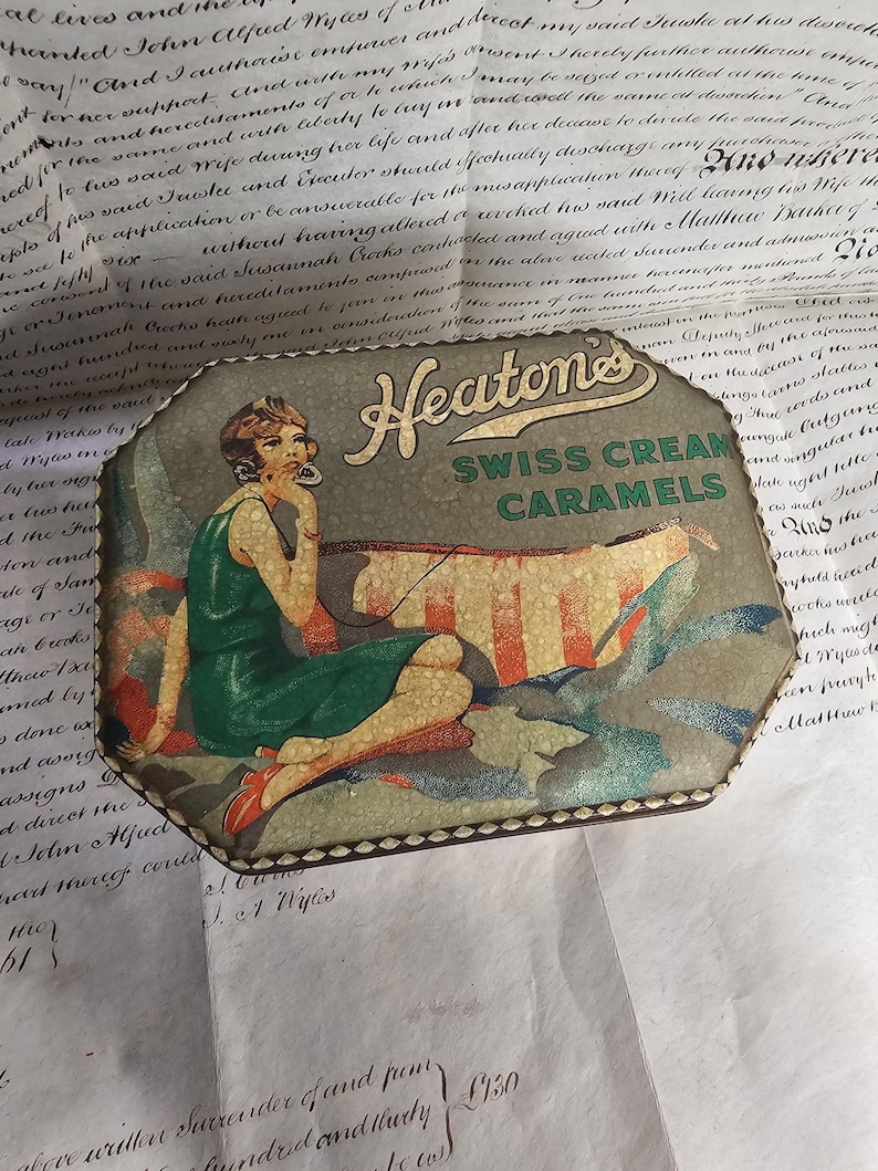 May include: Vintage Heatone's Swiss Cream Caramels tin. The tin features an illustration of a woman in a green dress, red shoes, and a stylish bob haircut. The tin is octagonal and has a decorative border.