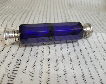 May include: A cobalt blue glass bottle with a silver stopper. The bottle is rectangular in shape and has a faceted design.