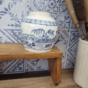 May include: A small, white ceramic jar with a blue and white floral design. The jar is sitting on a wooden shelf.