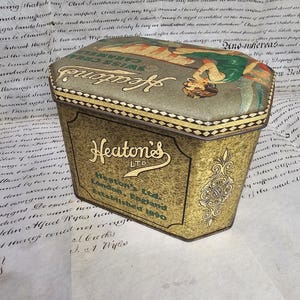 May include: Vintage Heaton's LTD Swiss Cream Caramels tin. The tin has a gold and green color scheme with an illustration on the lid. The text "Heaton's LTD London, England Established 1890" is visible on the tin.