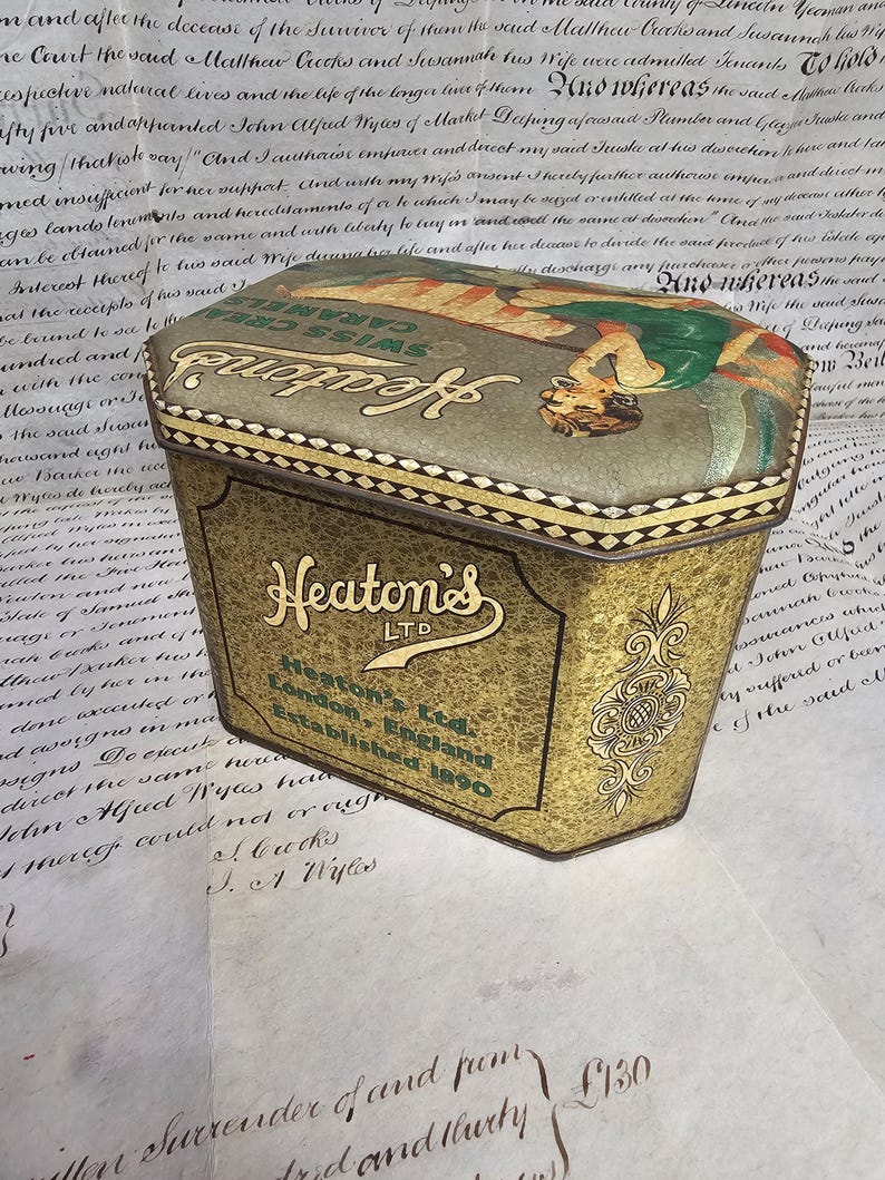 May include: Vintage Heaton's LTD Swiss Cream Caramels tin. The tin has a gold and green color scheme with an illustration on the lid. The text "Heaton's LTD London, England Established 1890" is visible on the tin.