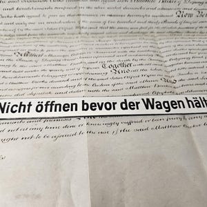 Può includere: Un cartello rettangolare in metallo bianco con testo nero che recita "Nicht öffnen bevor der Wagen hält" (Non aprire prima che la carrozza si fermi). Il cartello è su uno sfondo di carta invecchiata con scrittura manoscritta.