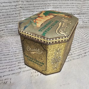 May include: Vintage Heaton's Swiss Cream Caramels tin. The tin has a gold and green color scheme with ornate detailing. The top features an illustration of a woman. The text "Choice Swiss Cream Caramels" is visible.