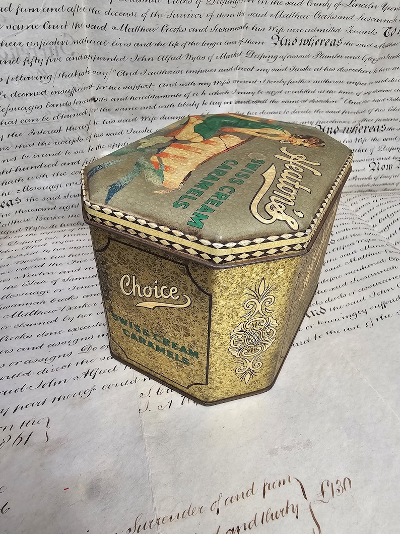 May include: Vintage Heaton's Swiss Cream Caramels tin. The tin has a gold and green color scheme with ornate detailing. The top features an illustration of a woman. The text "Choice Swiss Cream Caramels" is visible.