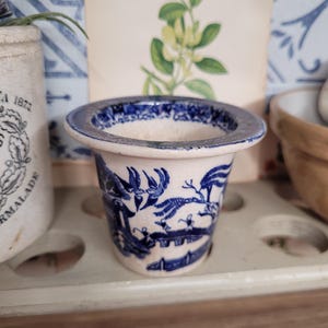 Könnte beinhalten: Ein kleiner weißer Keramiktopf mit einem blauen und weißen Blumenmuster. Der Topf hat einen breiten Rand und eine schmale Basis.