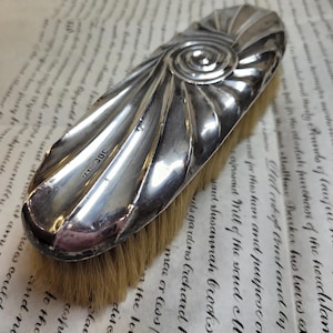 May include: A silver-plated brush with a swirling design on the handle. The brush has a brown bristle head and the handle is marked with the number "300".